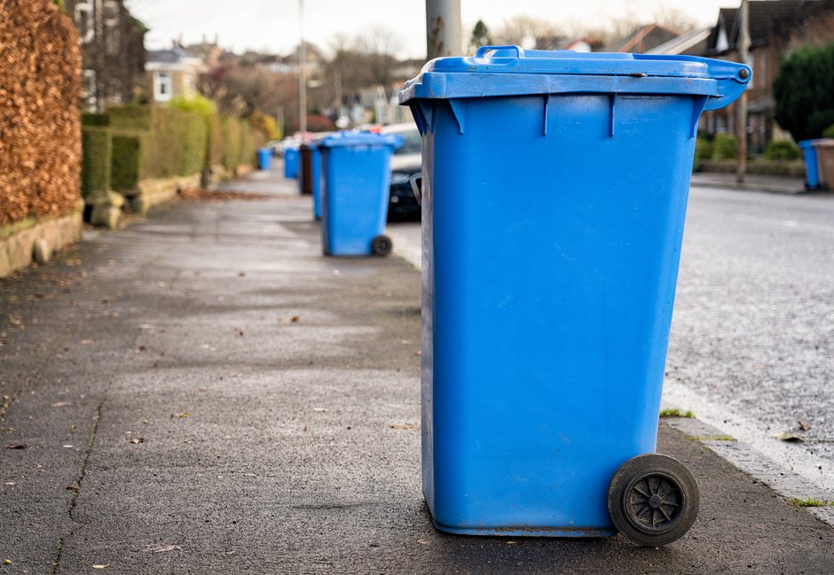 Mehrere blaue Mülltonnen stehen auf einem Fußgängerweg